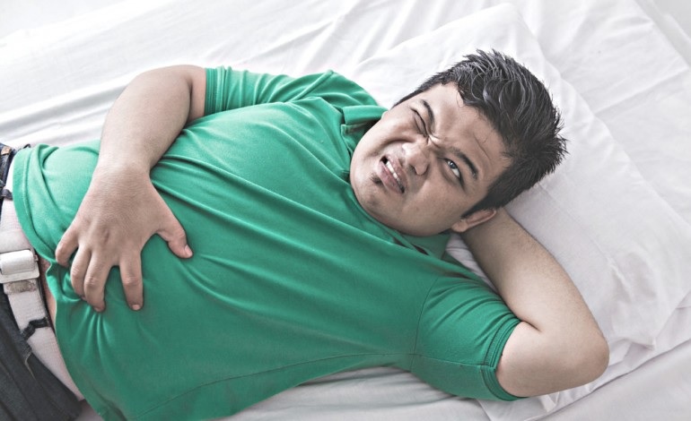 obese man in green tee shirt clutches his stomach